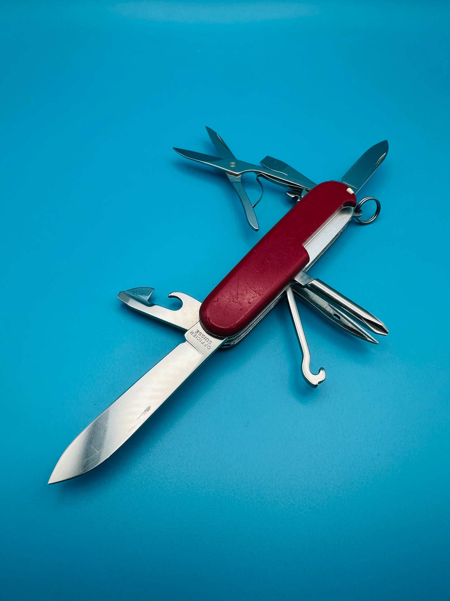 Red Swiss Army knife Super Tinker fully opened, laying on blue surface