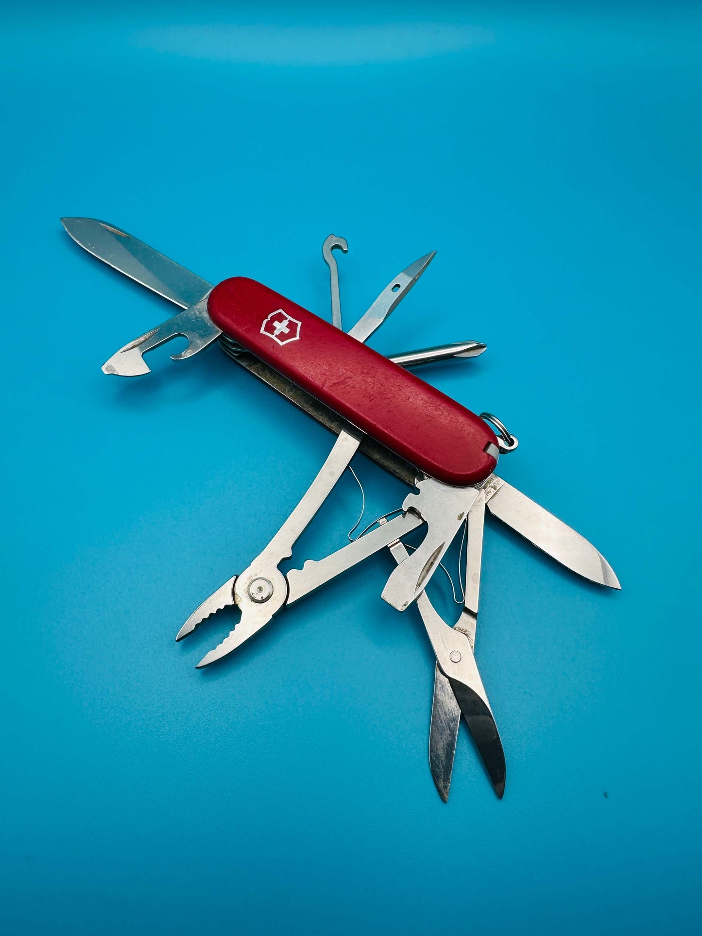Red Victorinox Deluxe Tinker multitool with all tools extended on blue background