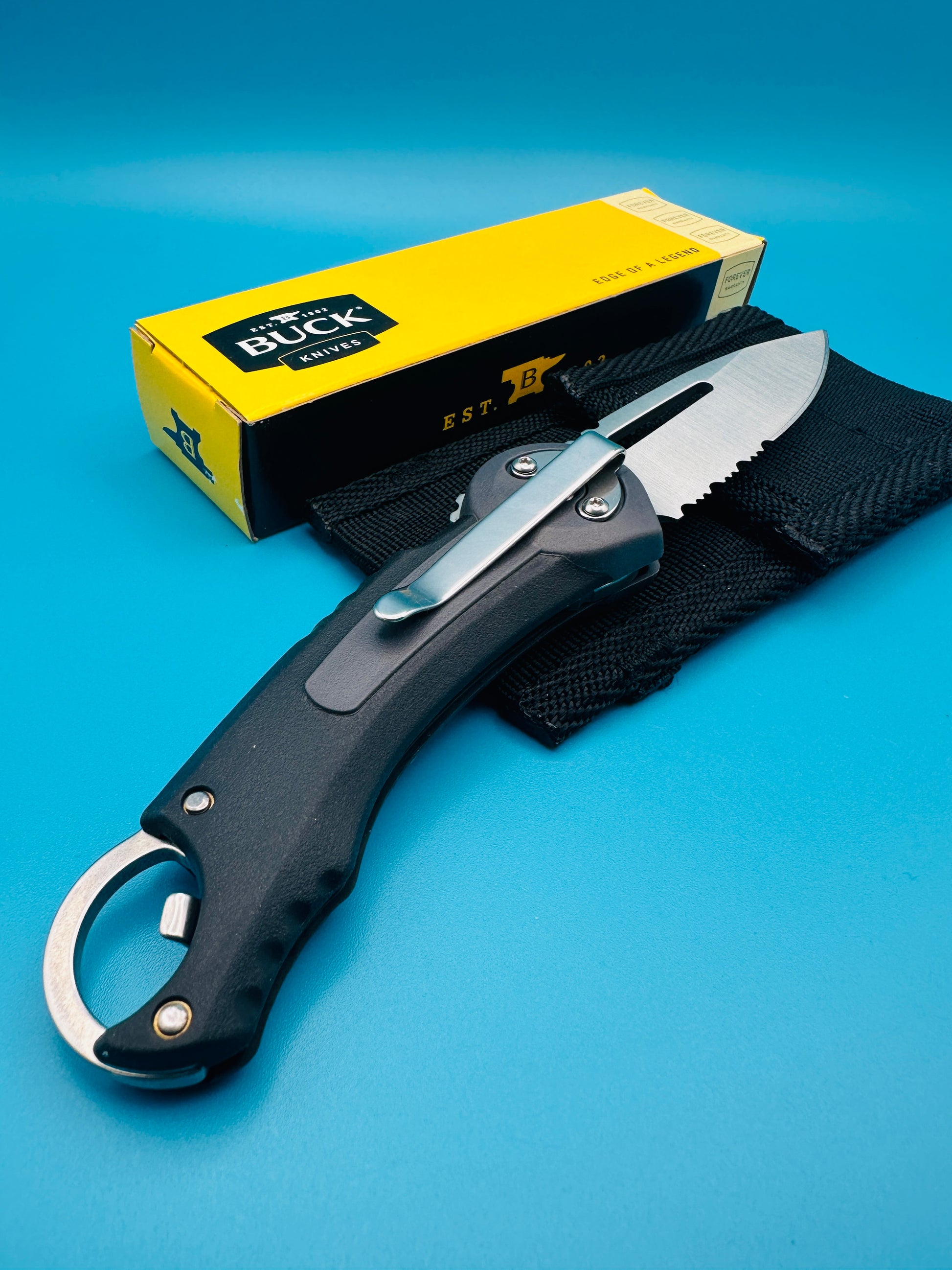 Buck Redpoint black folding knife folded with yellow box and sheath, on blue background.
