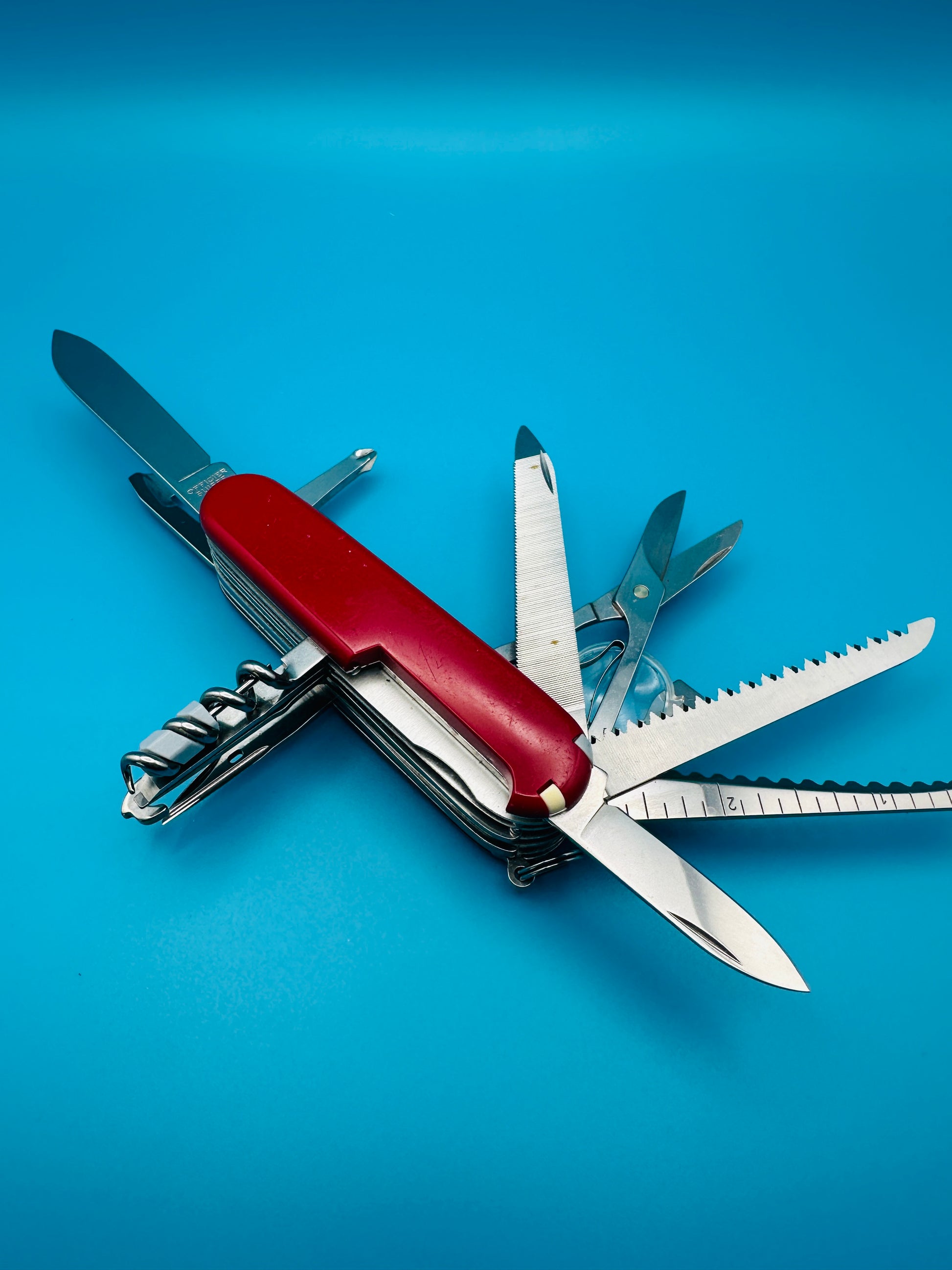 Multiple tools of Champion Plus Swiss Army knife unfolded on blue surface