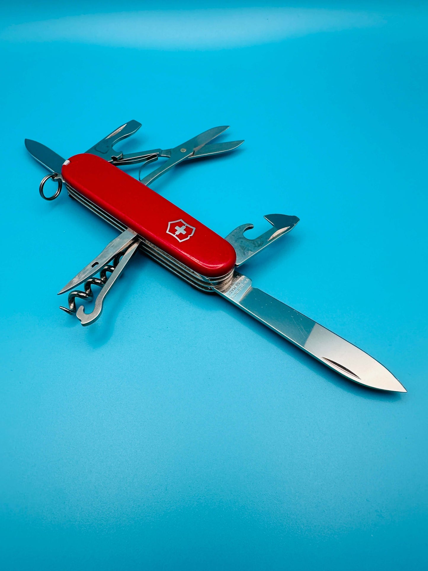 Victorinox Climber Swiss Army knife with tools fully extended, including large blade, scissors, corkscrew, and hook on a blue background