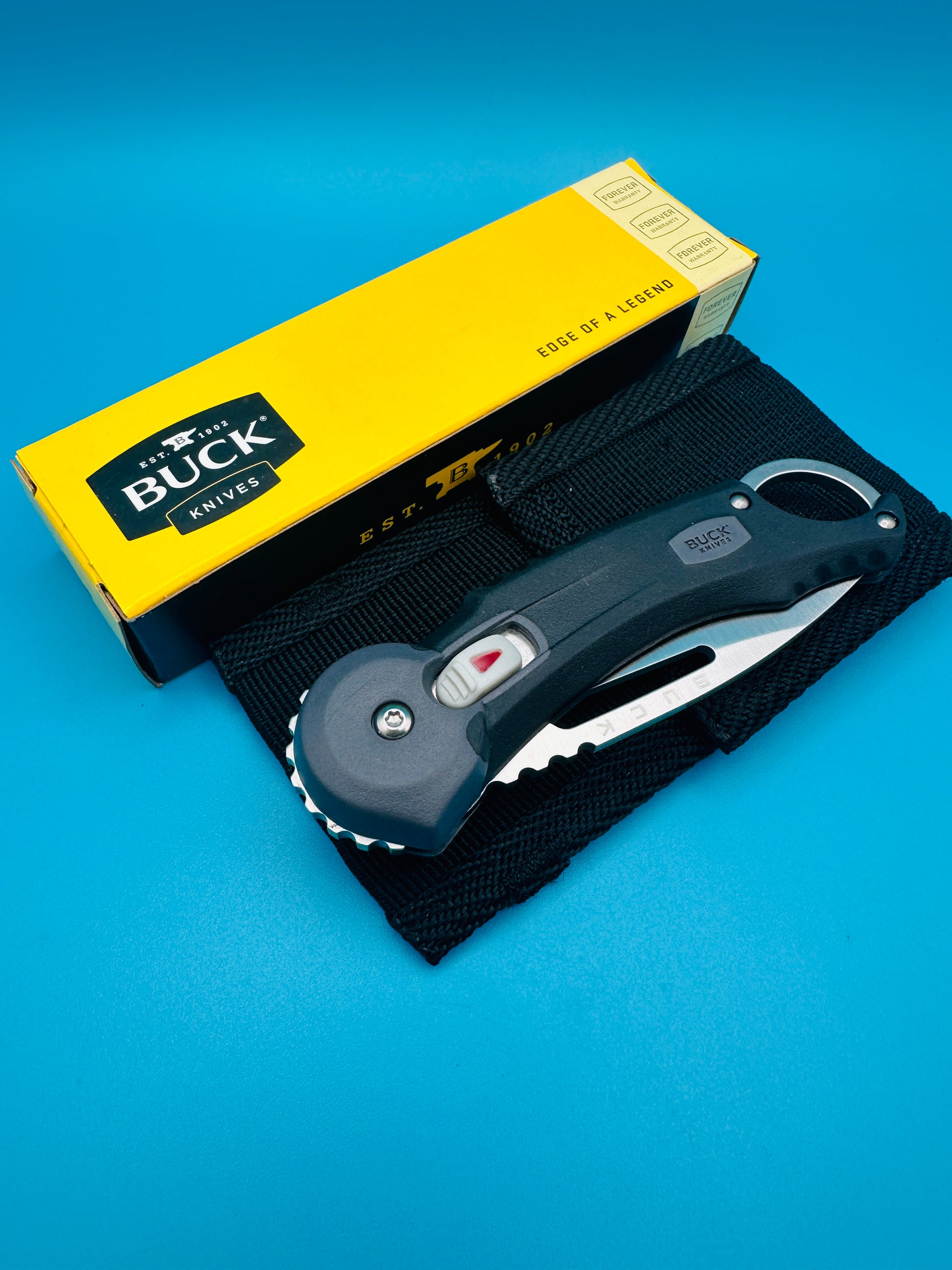 Buck Redpoint black folding knife with blade open and sheath, yellow box on blue background.