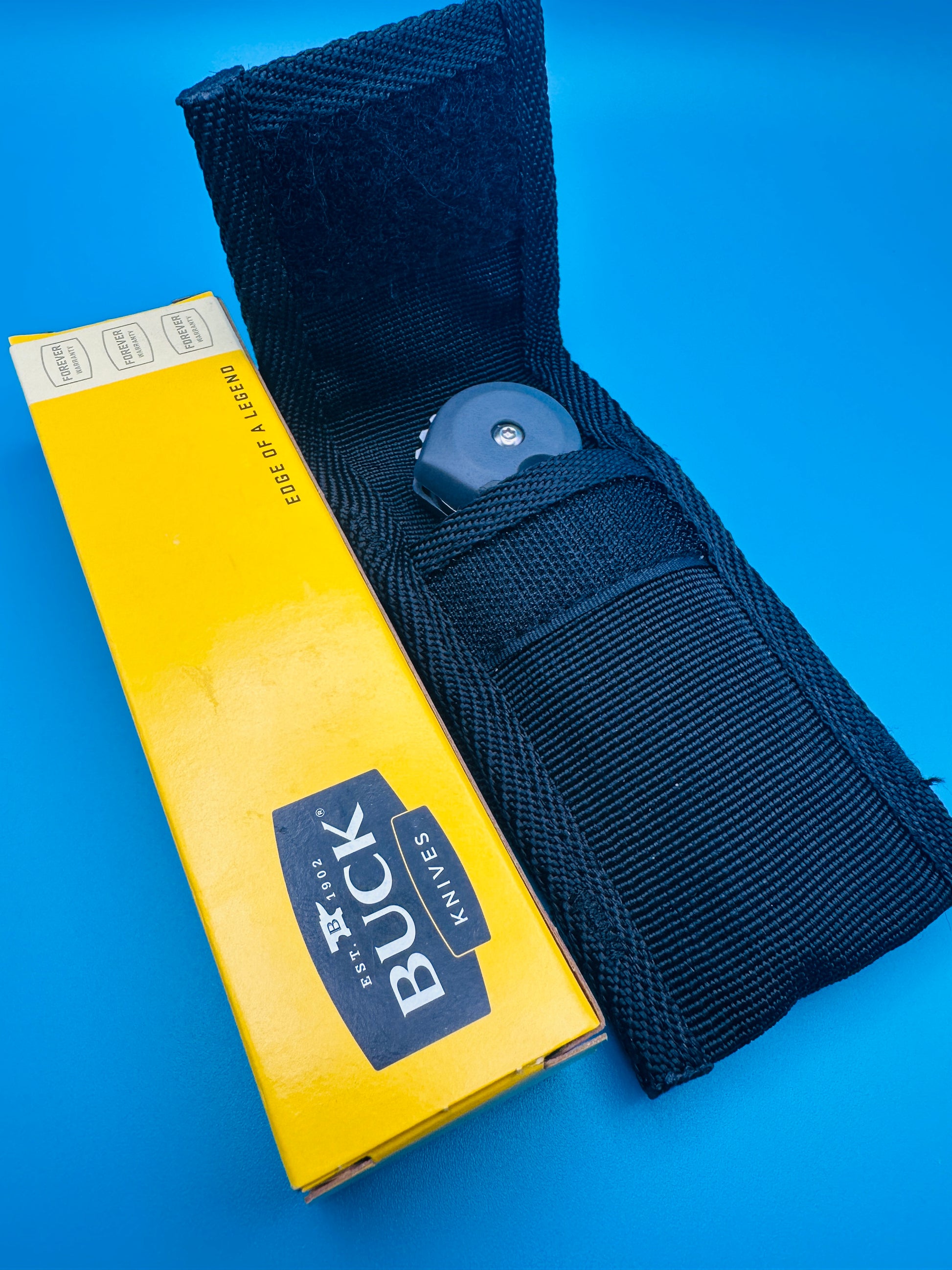 Buck branded nylon sheath with yellow box, on blue background.
