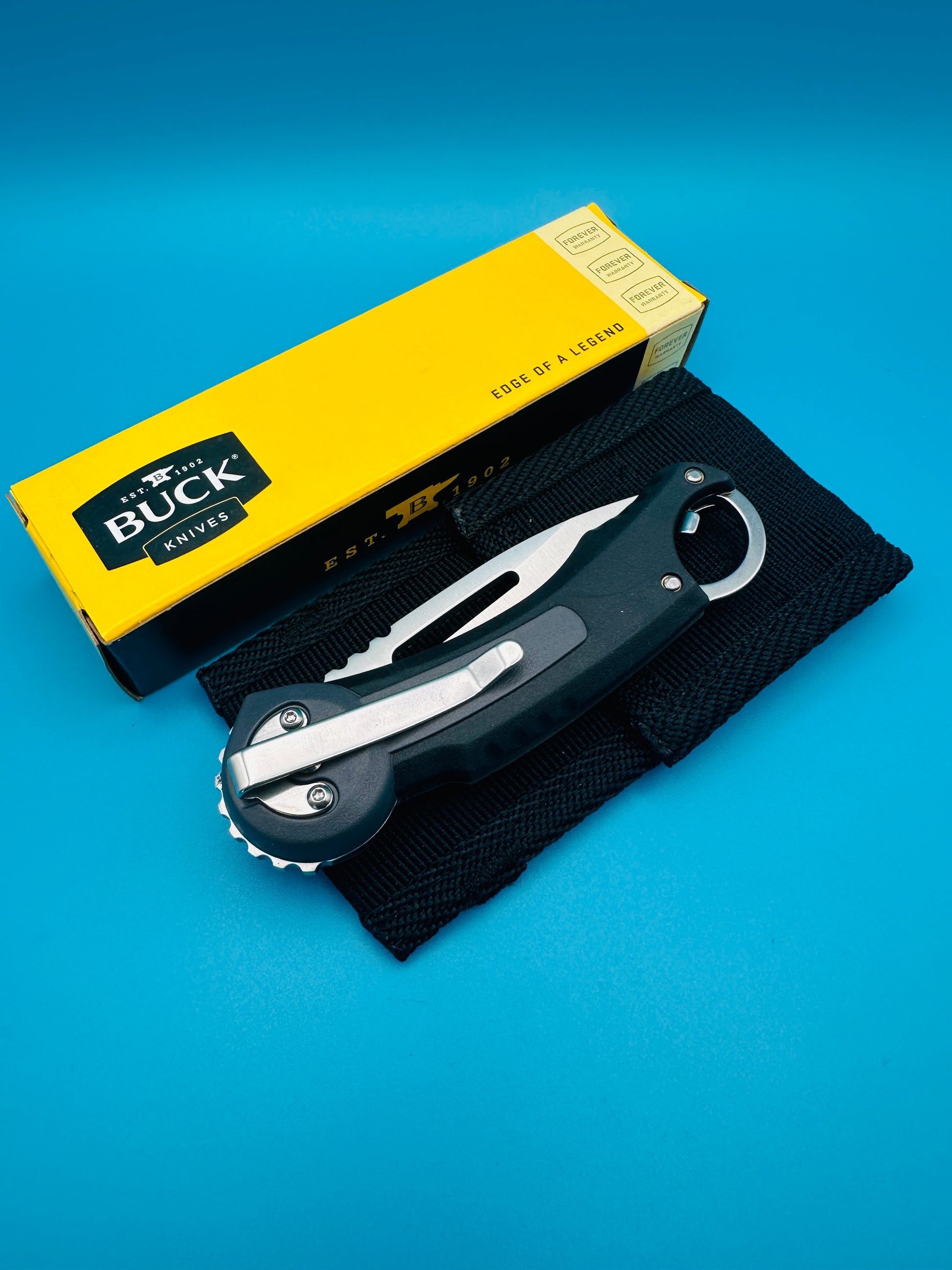 Buck Redpoint black folding knife folded with yellow box, on blue background.

